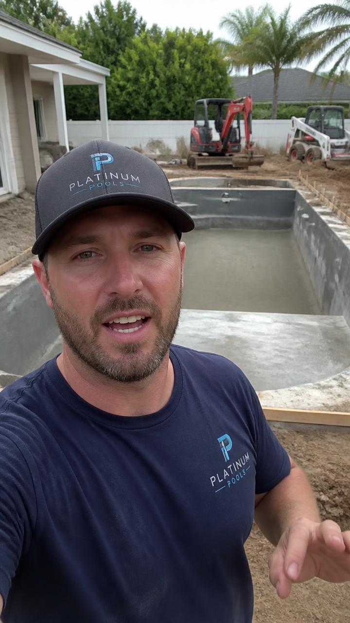 Pool builder in a cap filming a phone walk-through on a real job site